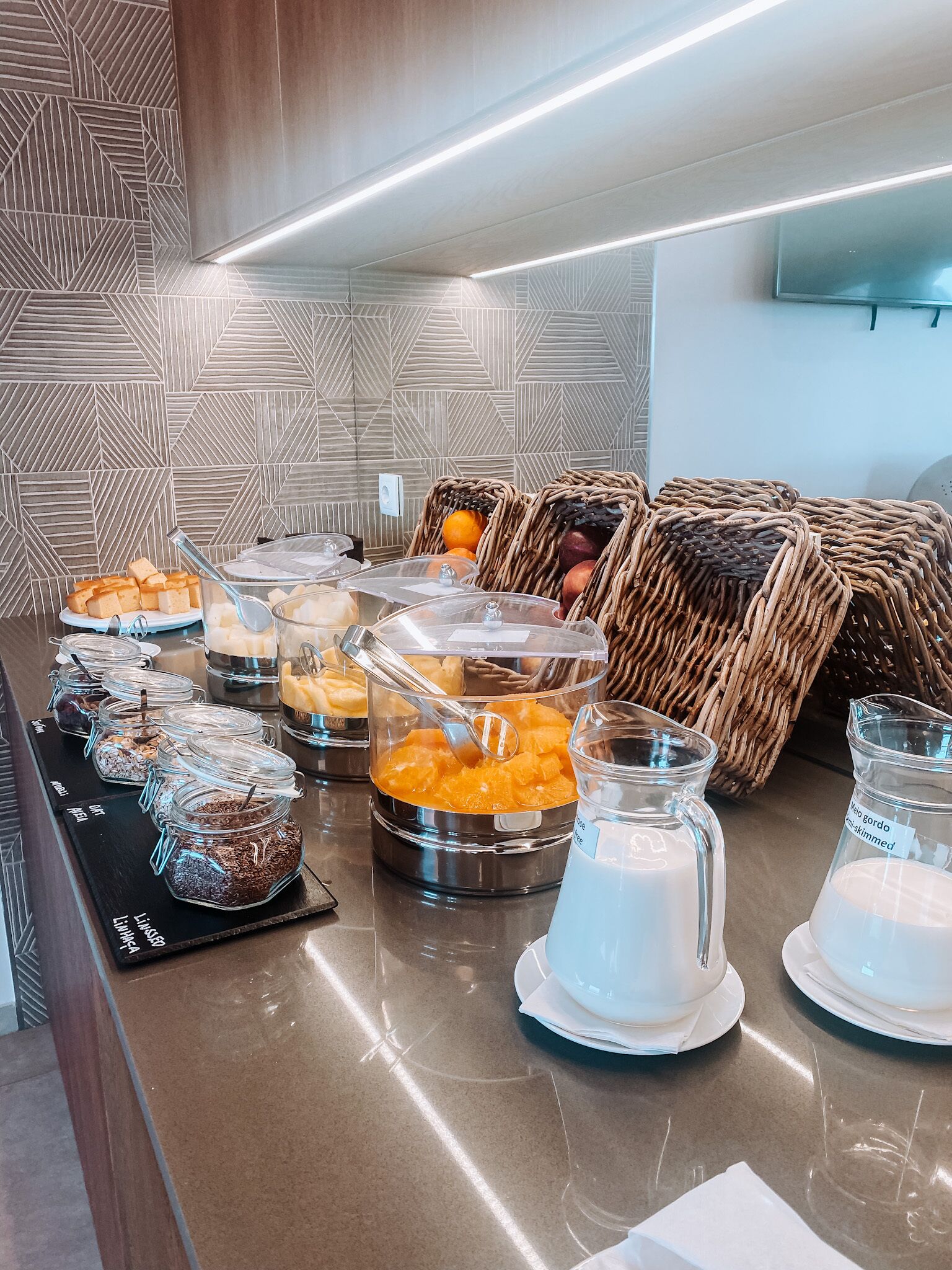 A buffet area with various food items, including jars of cereal, fruit, and a milk dispenser.