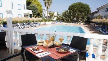 Zona de dinar a la piscina amb una taula preparada per a dues persones, amb vista a una piscina.