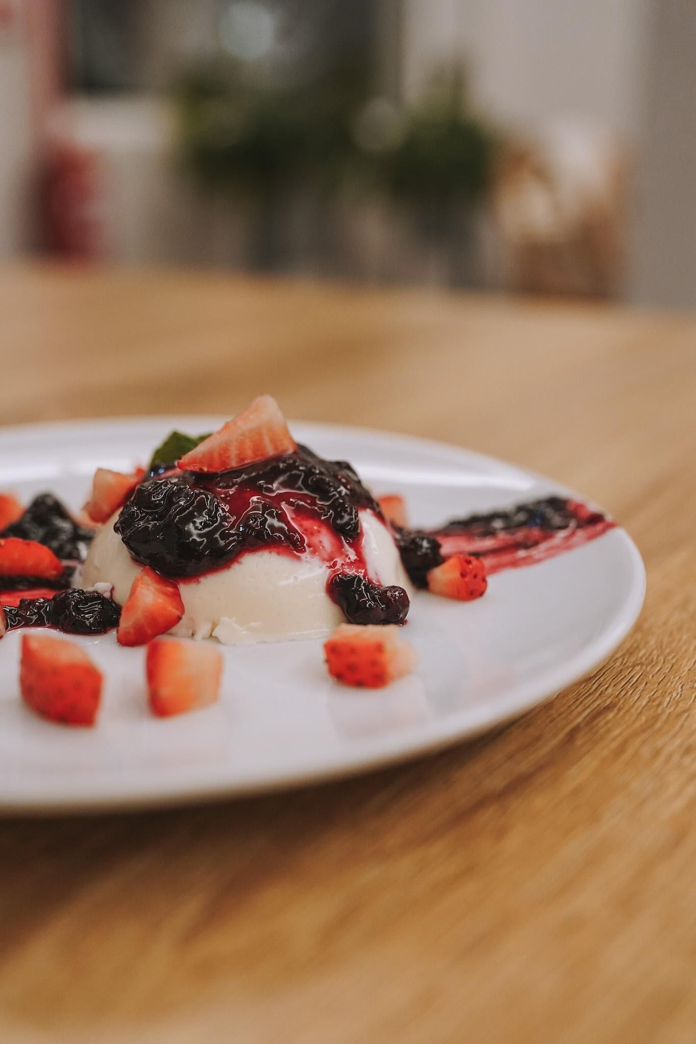 Dessert auf weißem Teller mit Erdbeeren und dunkler Sauce.