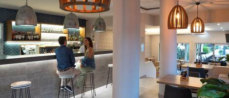 A modern bar area with high stools, pendant lighting, and a bar counter displaying bottles and glasses.