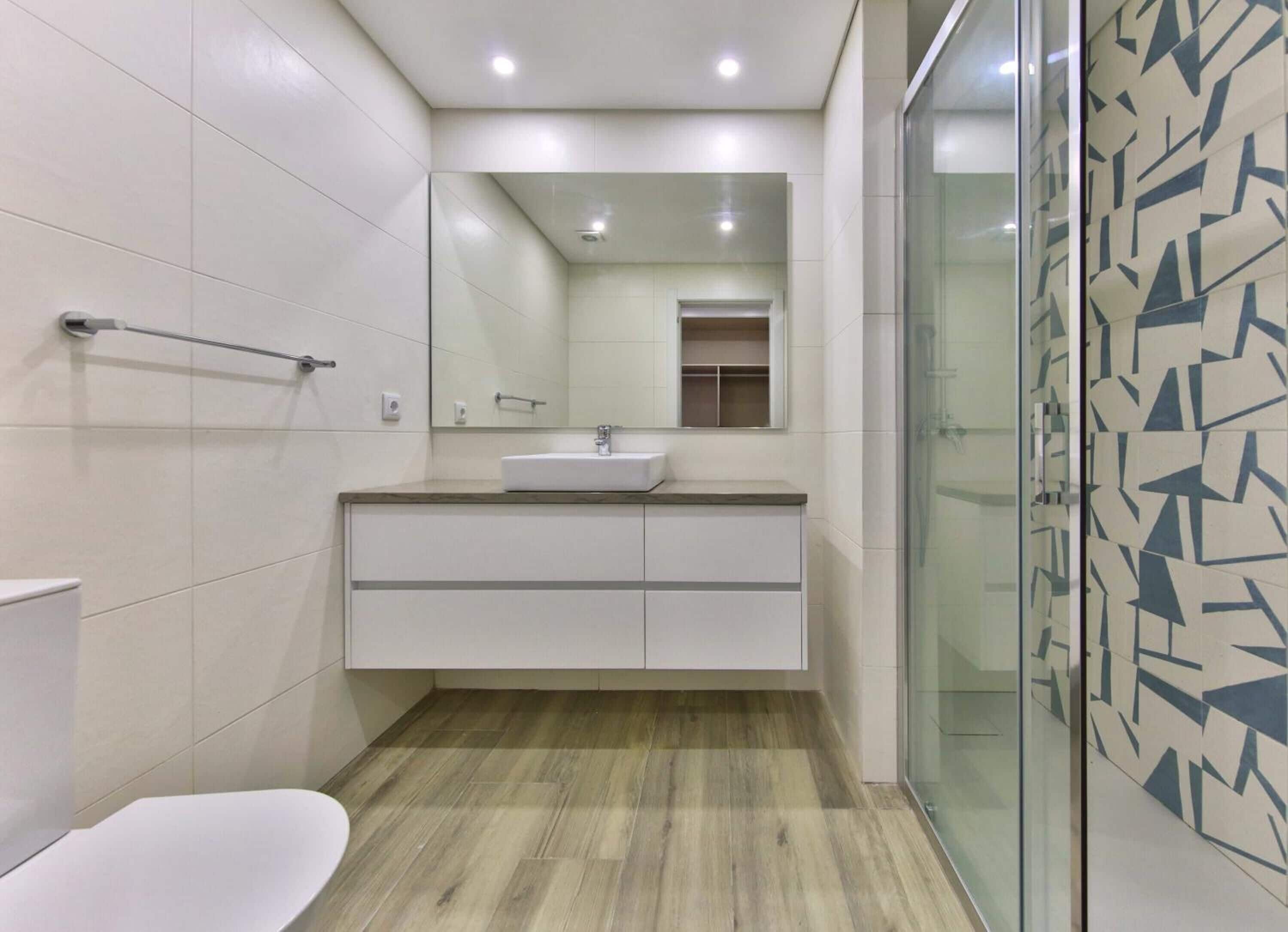 Un baño moderno con un lavamanos blanco, espejo y suelo de madera.