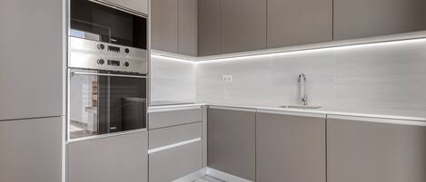 A modern kitchen with built-in appliances, a stainless steel sink, and a lighted backsplash.