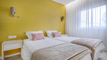 A hotel room with two beds, a yellow accent wall, and a large window with sheer curtains.