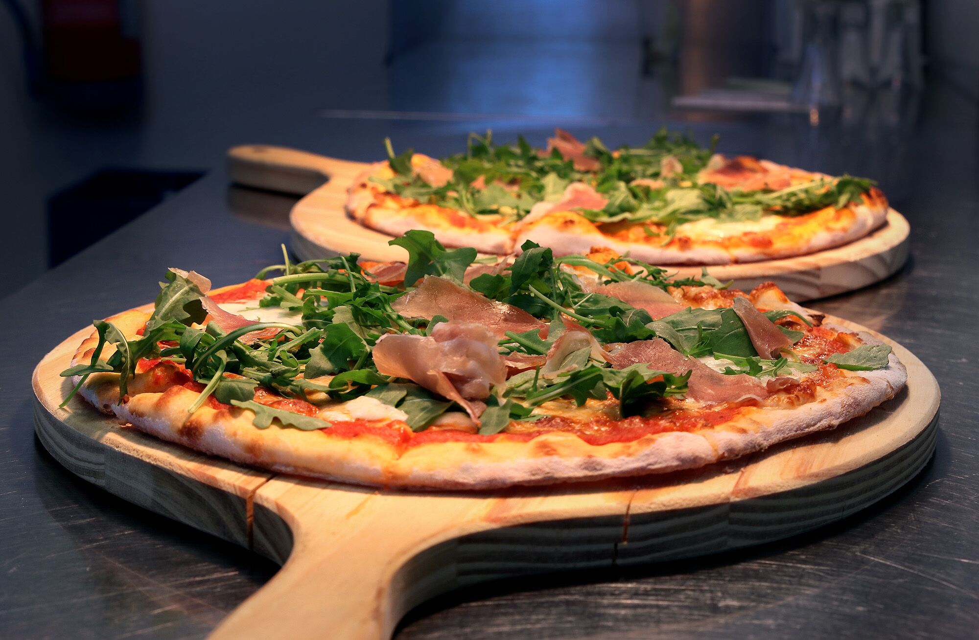 Dos pizzas sobre tablas de madera, con un fondo oscuro.