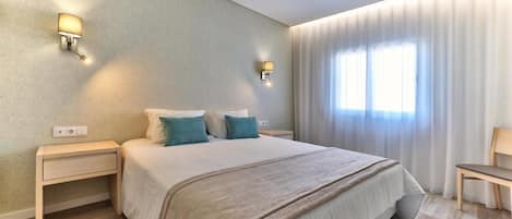 A modern hotel room with a large bed, two bedside tables, a nightstand, and a chair.