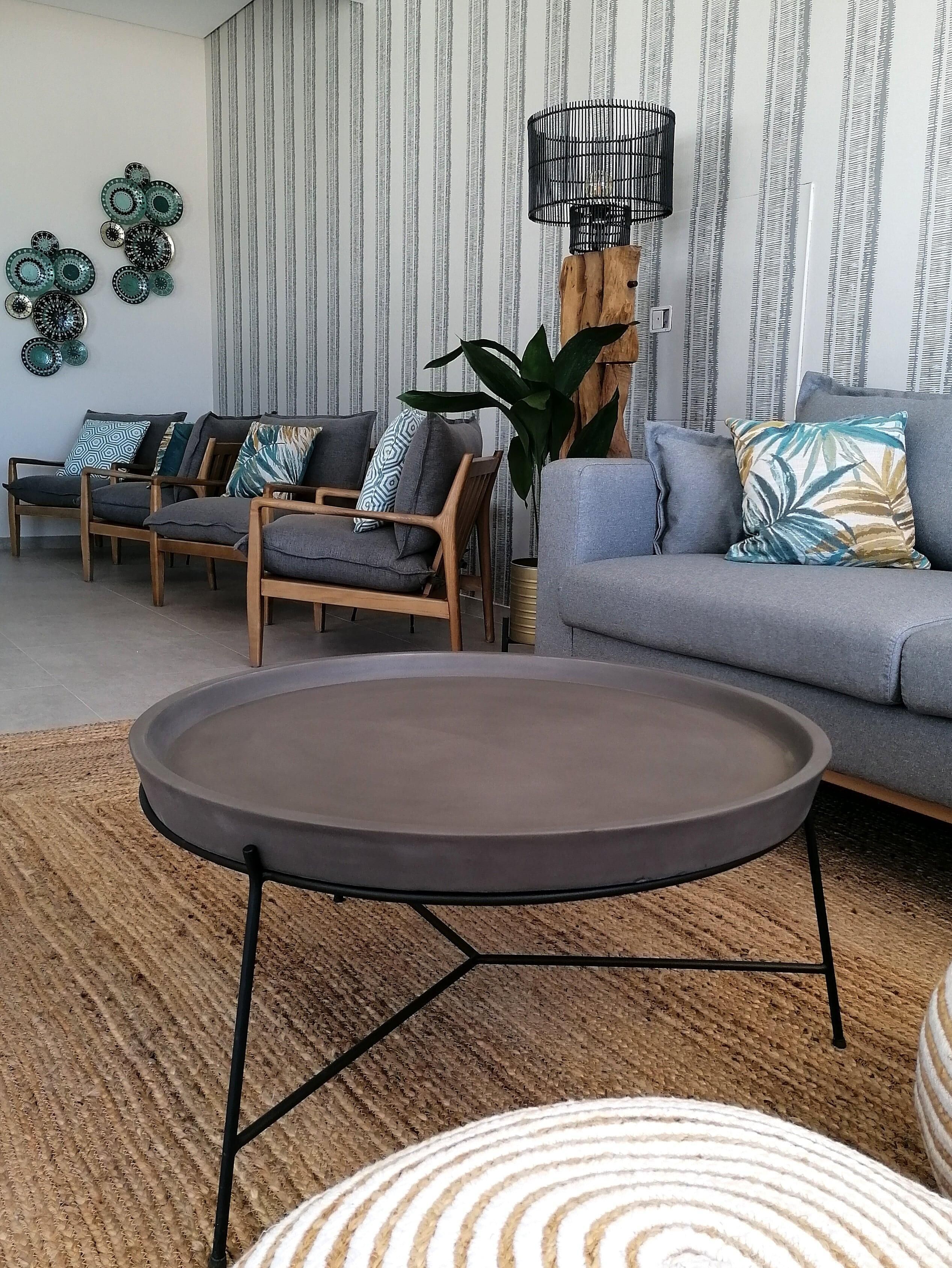 Una sala de estar moderna con un sofá gris, sillas de madera, una mesa de centro redonda y un papel tapiz a rayas.