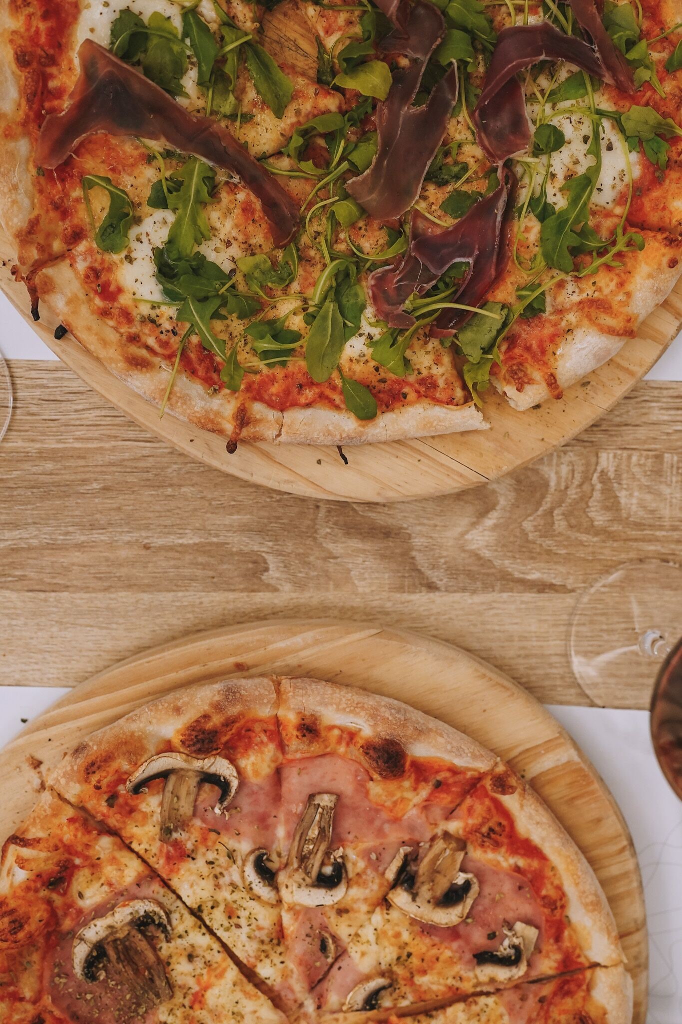 Twee pizza's op houten planken, één met groenten en de ander met champignons en ham.