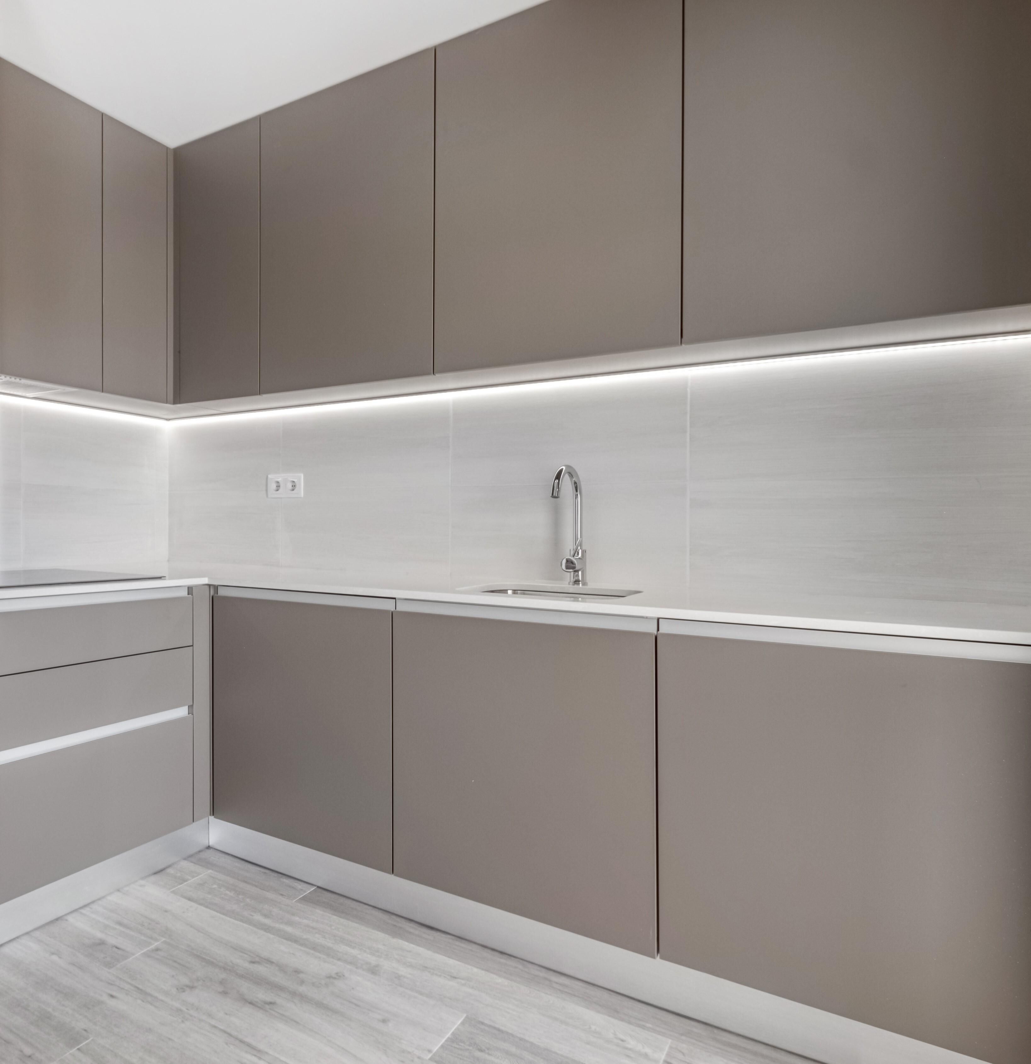 Una cocina moderna con armarios grises, un lavamanos de acero inoxidable y una encimera blanca.