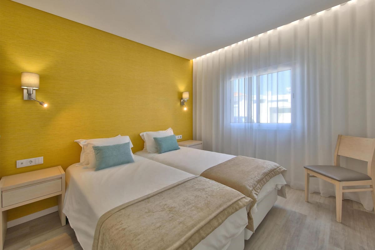 Habitación de hotel con dos camas, una silla y un ventanal con cortinas.