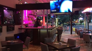 A bar area with a neon sign, seating, and a view of the street outside. - Hotel Devamlı (Marmaris)