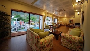A hotel lobby with floral-patterned sofas, a wooden coffee table, and a large window offering a view of the street outside. - Hotel Devamlı (Marmaris)