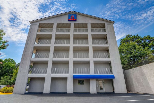 A multi-story hotel with a flat facade, balconies on each floor, and a blue awning over the entrance.