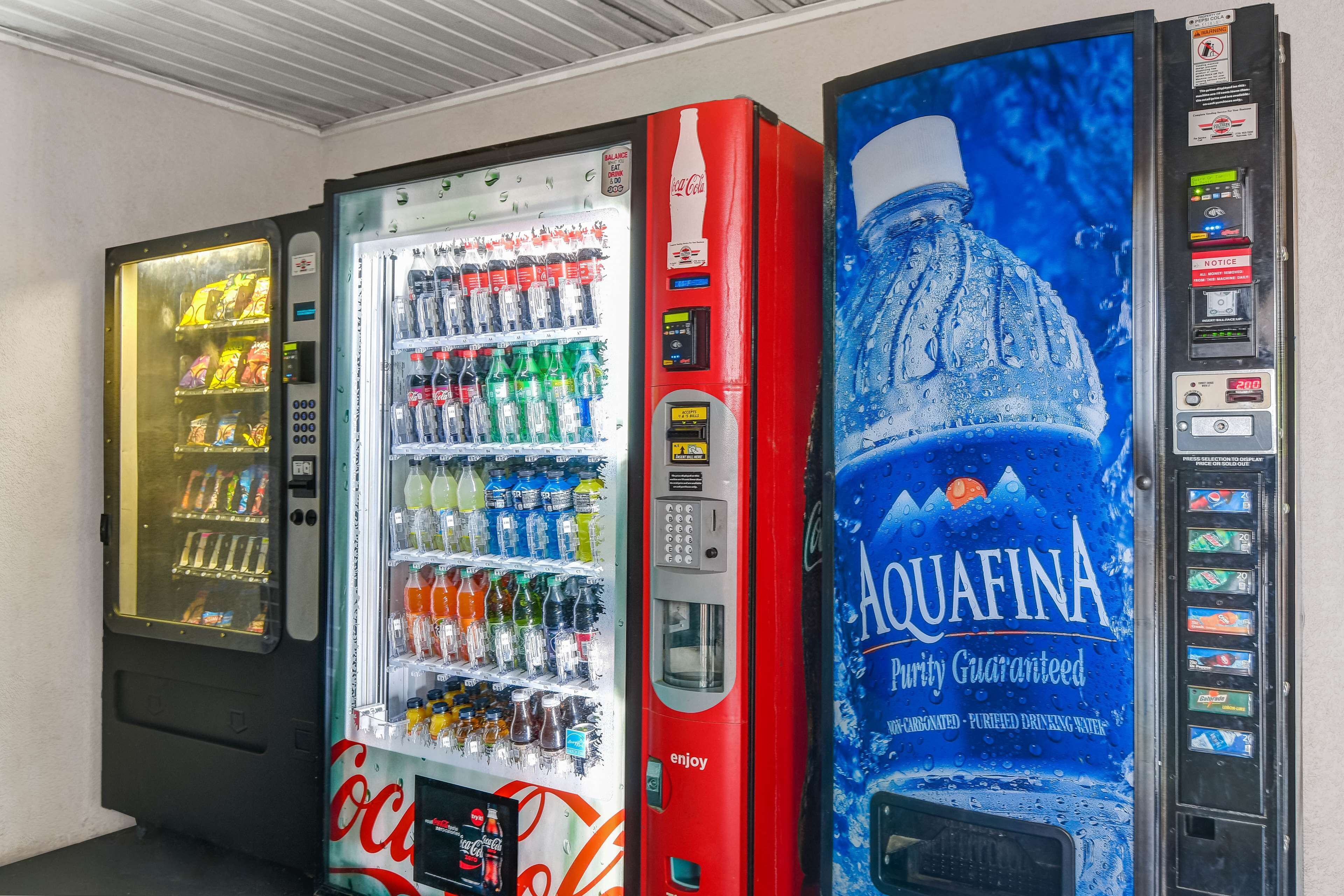 Three beverage vending machines, including Coca-Cola and Aquafina, in a commercial setting.