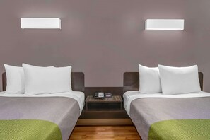 A hotel room with two beds, a small bedside table with a phone and a clock, and a wall-mounted light fixture.