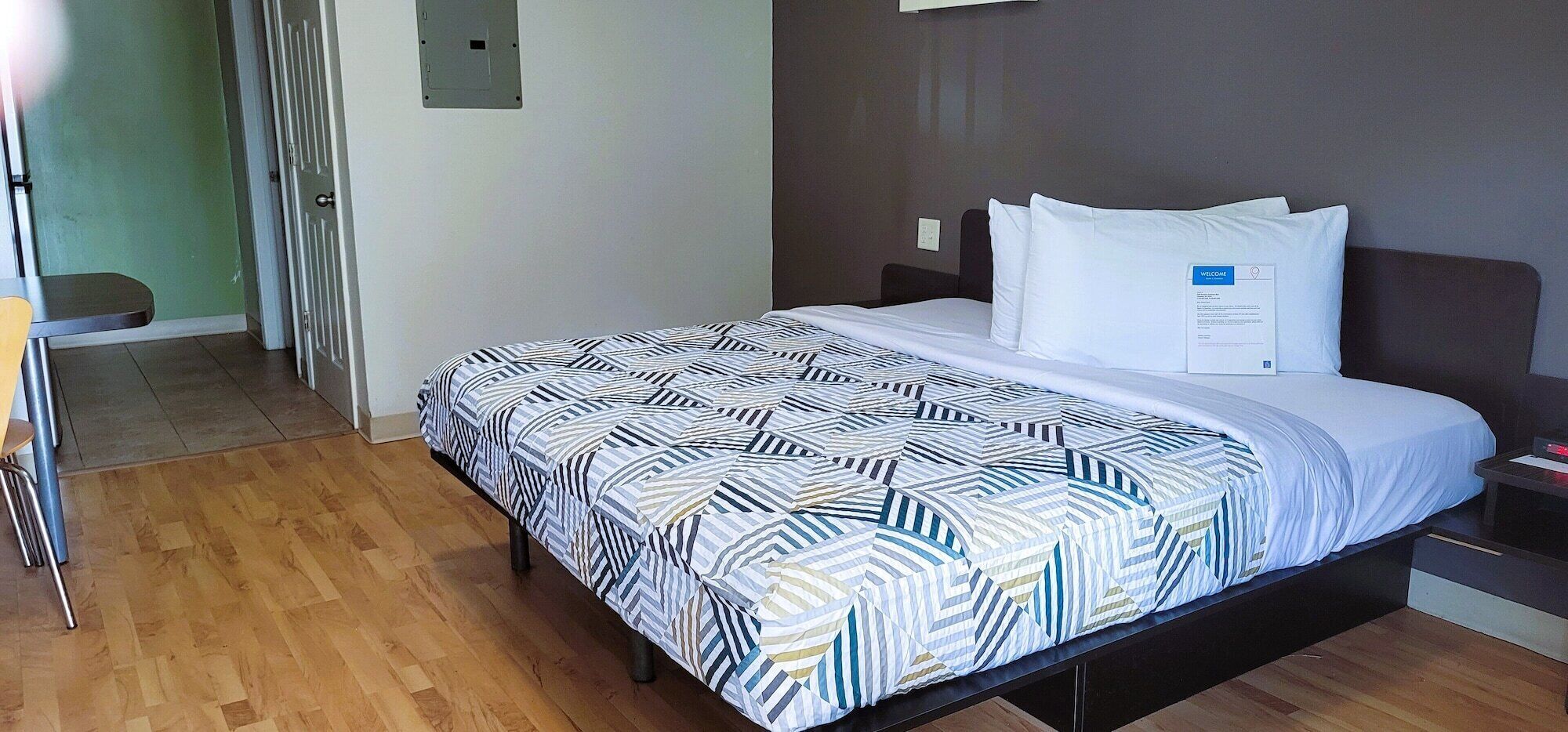 A hotel room with a bed, a bedside table, a chair, and a wooden floor.