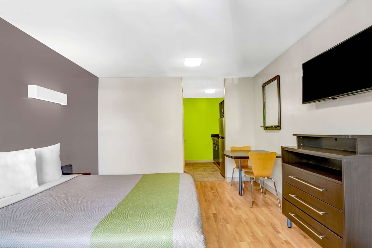 A modern hotel room with a bed, a desk, a chair, a TV, and a dresser.