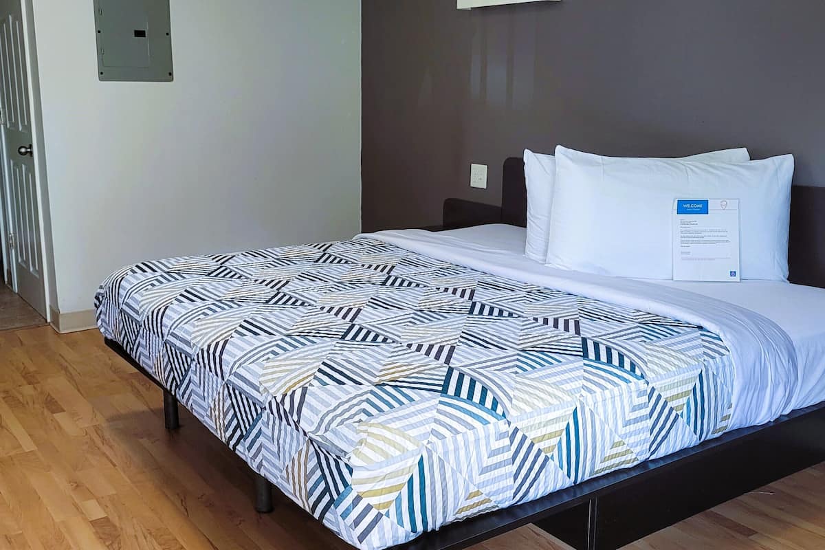 A hotel room with a bed, a bedside table, a chair, and a wooden floor.