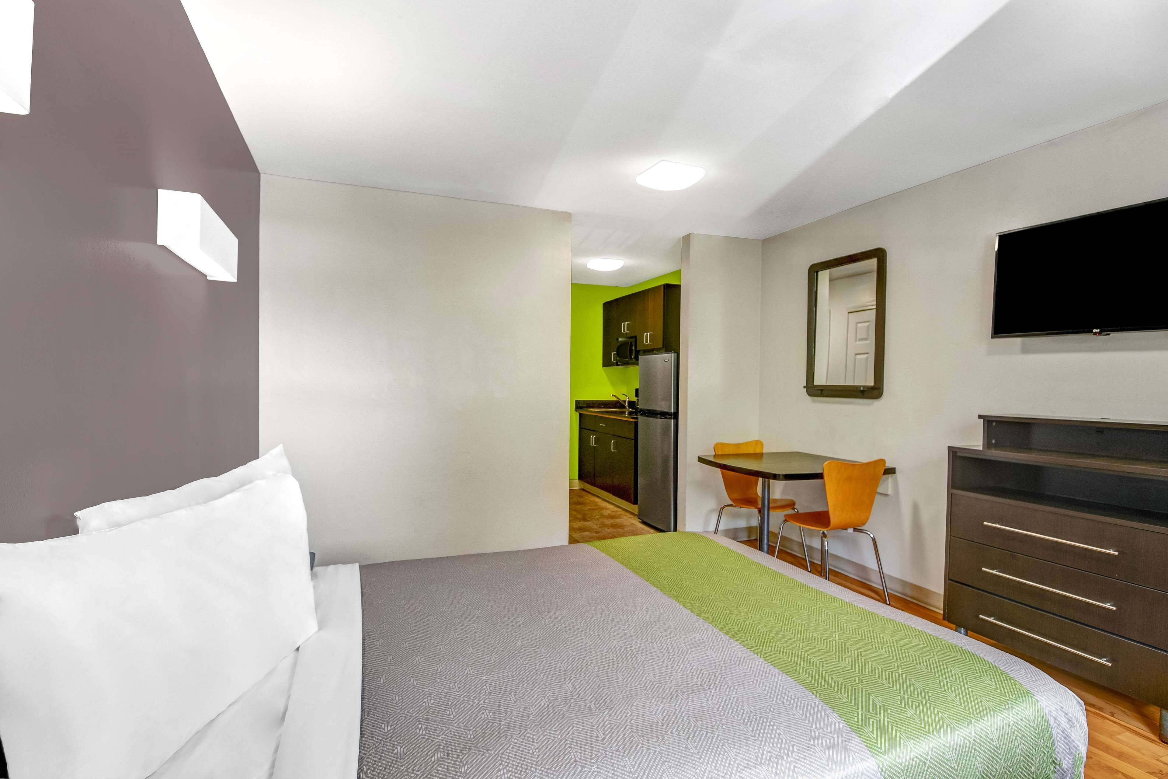 Una habitación de hotel con cama, escritorio, silla, televisor y armario.