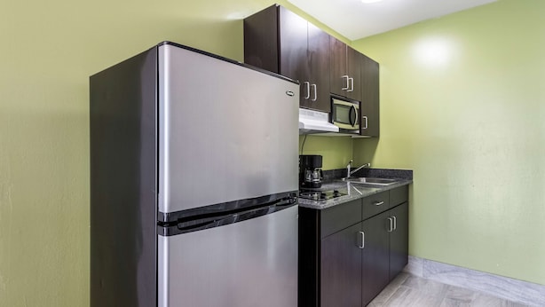 A compact kitchen with a stainless steel refrigerator, a microwave, and dark wooden cabinets. - Studio 6 Extended Stay - Savannah, GA (Savannah)