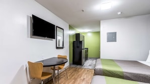 A compact hotel room with a bed, a small table with chairs, a TV mounted on the wall, and a refrigerator. - Studio 6 Extended Stay - Savannah, GA (Savannah)