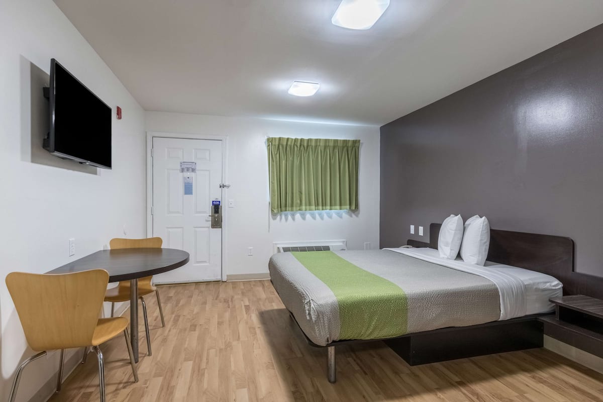 Habitación de hotel con cama, escritorio, silla, televisor y ventana con cortinas.
