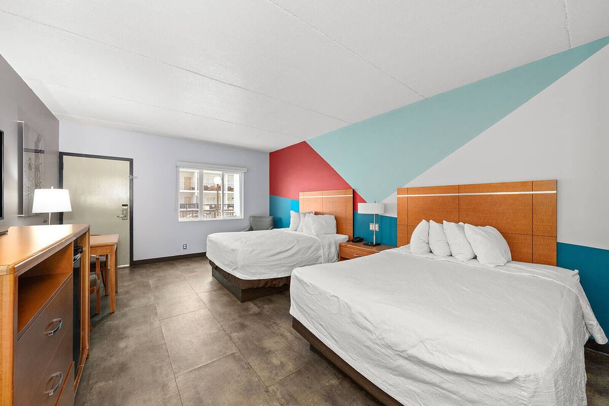A hotel room with two beds, a desk, and a window.