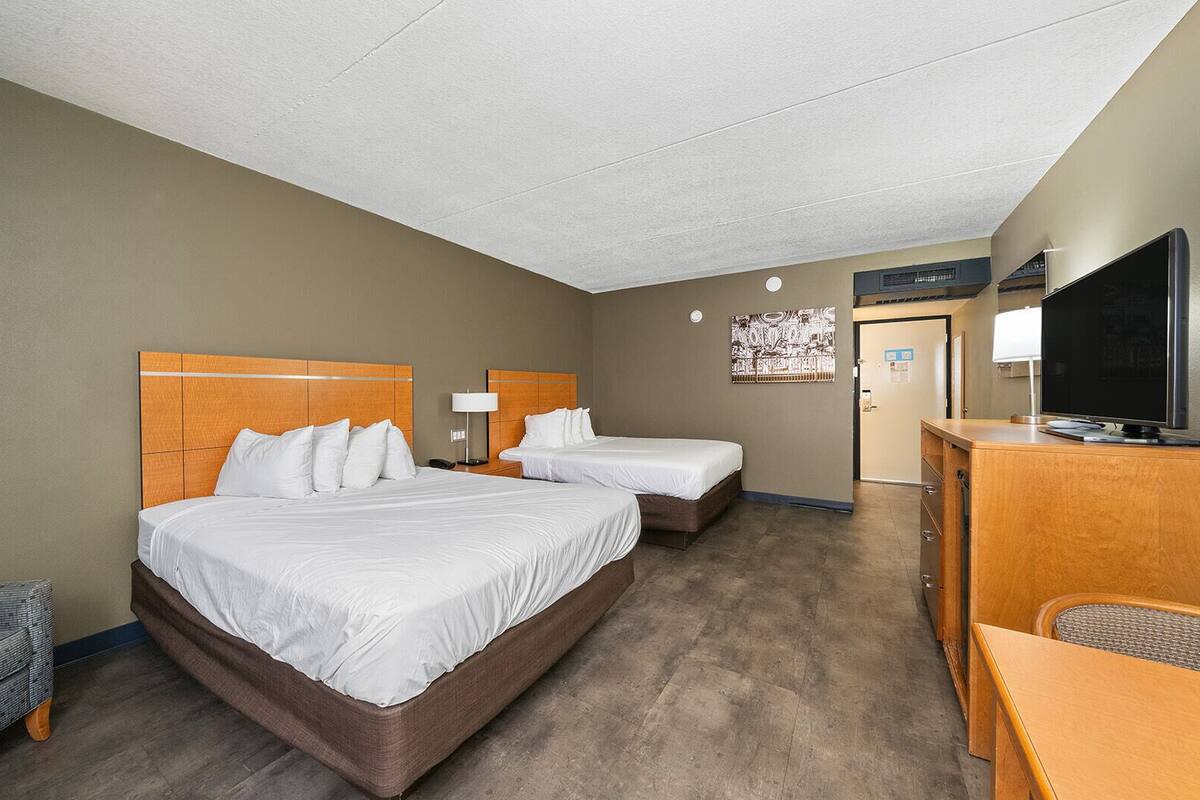 A hotel room with two beds, a desk, a television, and a door leading to a bathroom.
