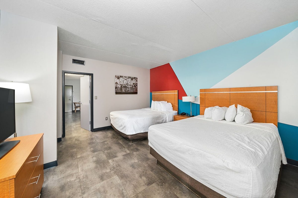 A hotel room with two beds, a TV, a desk, and a bathroom visible through an open door.