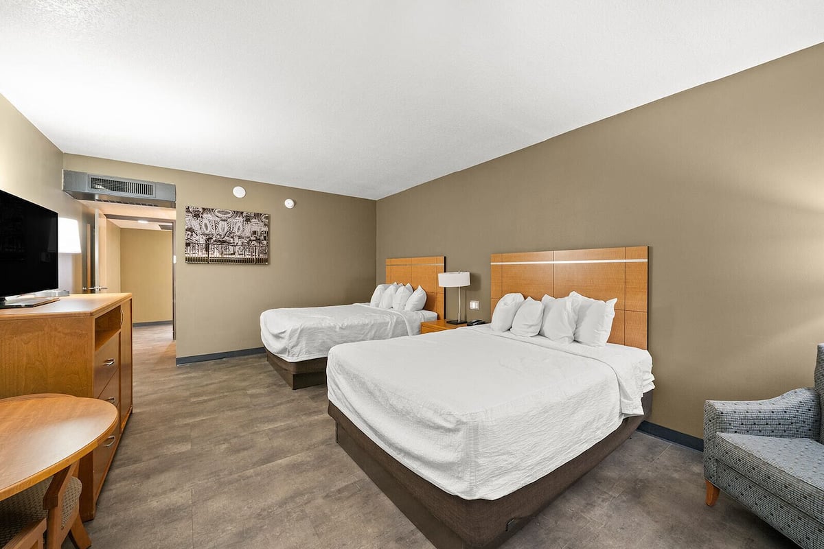 A hotel room with two beds, a desk, a chair, and a television.