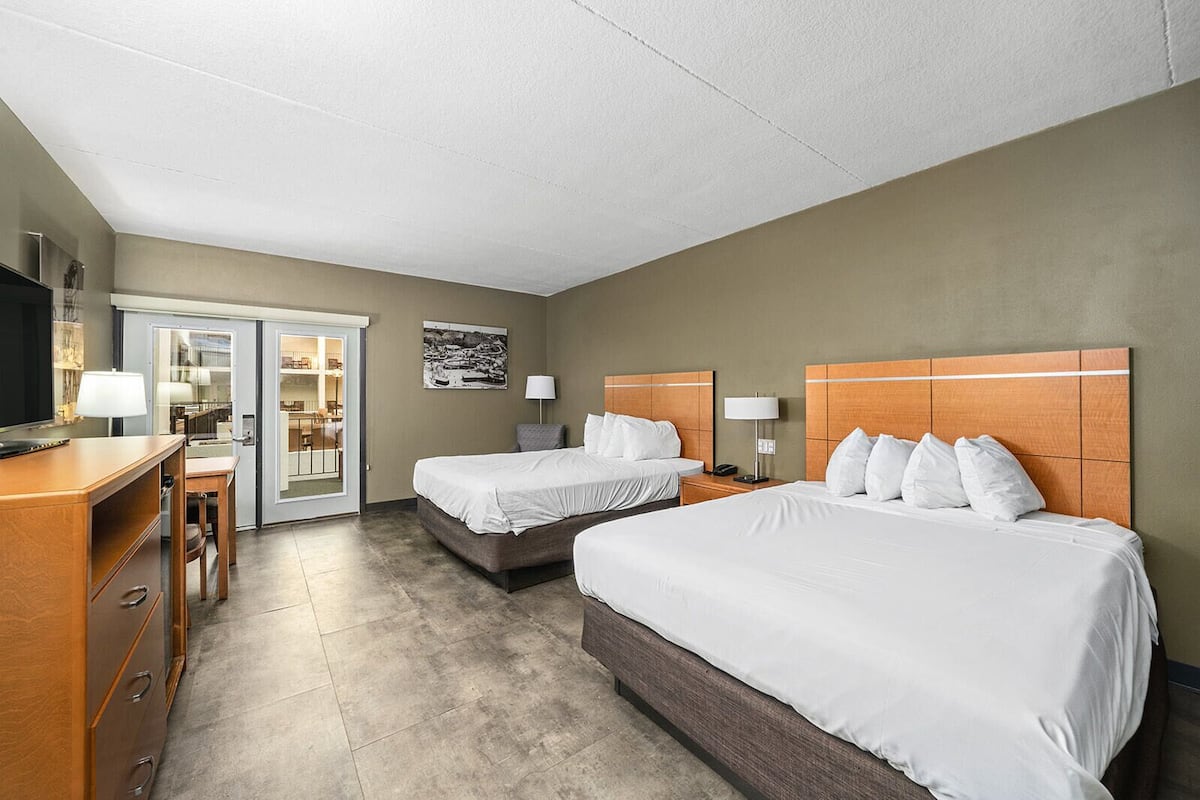 A hotel room with two beds, a desk with a chair, a television, and a door leading to a balcony.