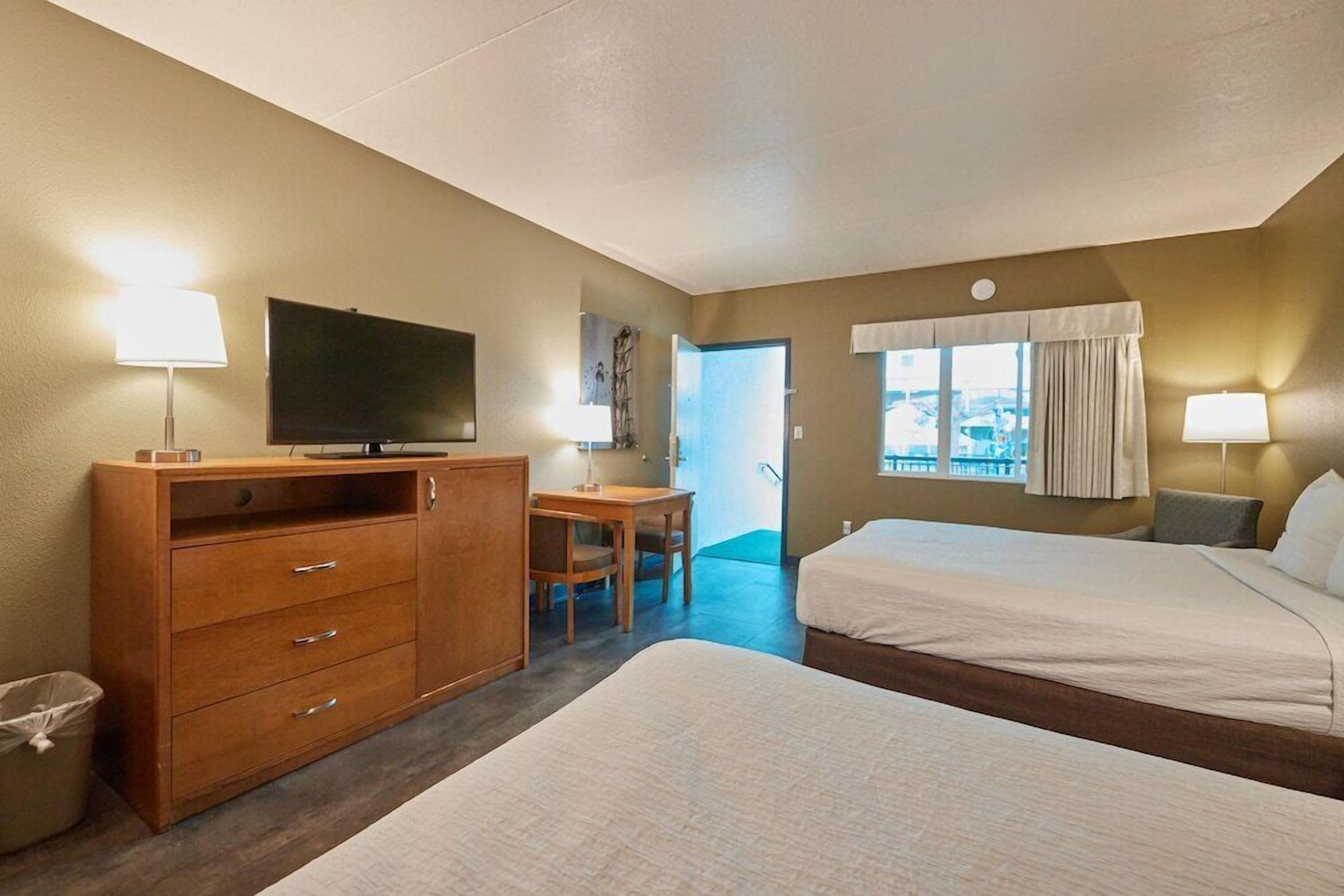A hotel room with two beds, a desk, a television, and a window with curtains.