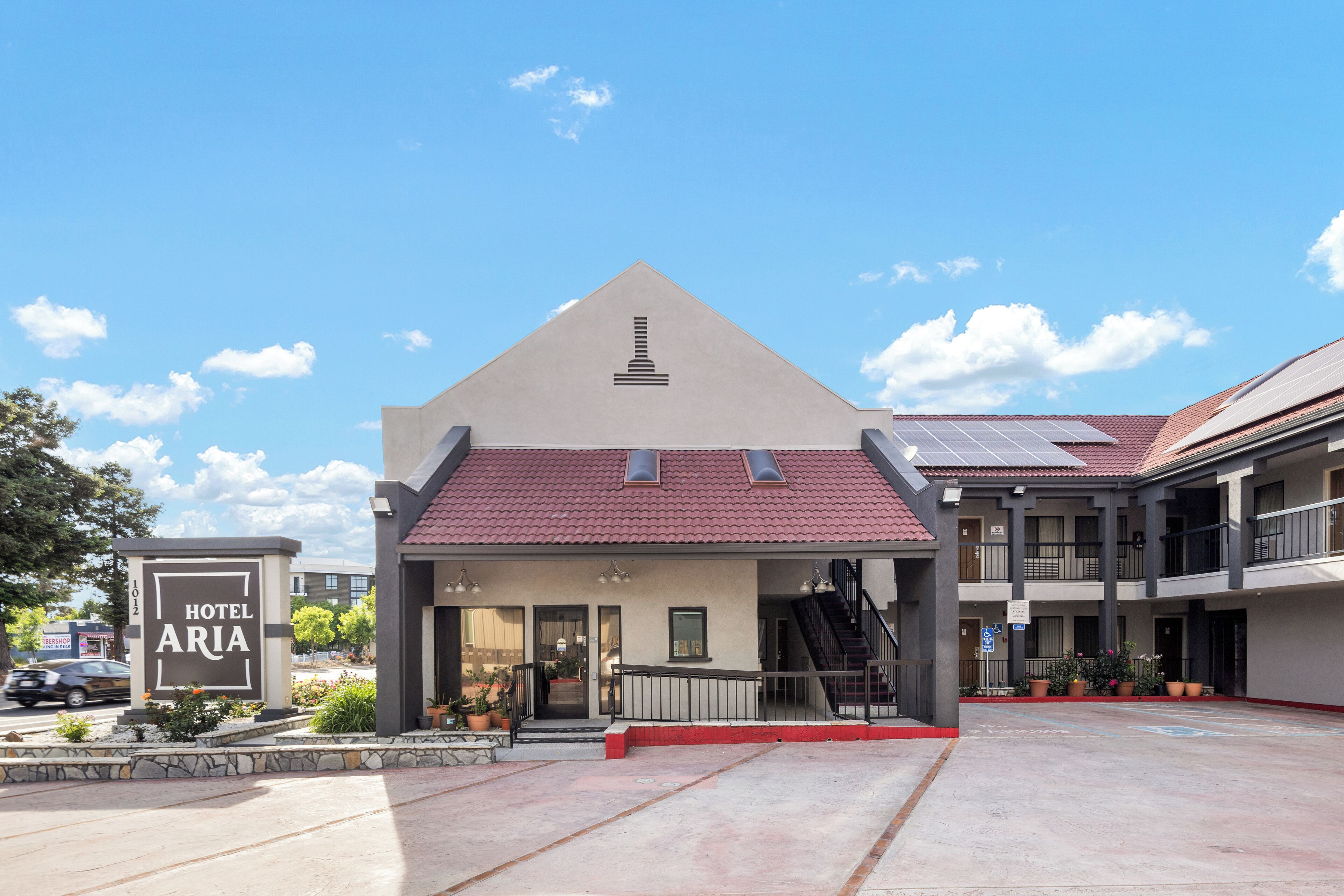 A hotel with a red-tiled roof, a signboard, and a parking area.
