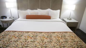 A hotel room with a neatly made bed, two bedside lamps, a clock, and a small table with a phone.
