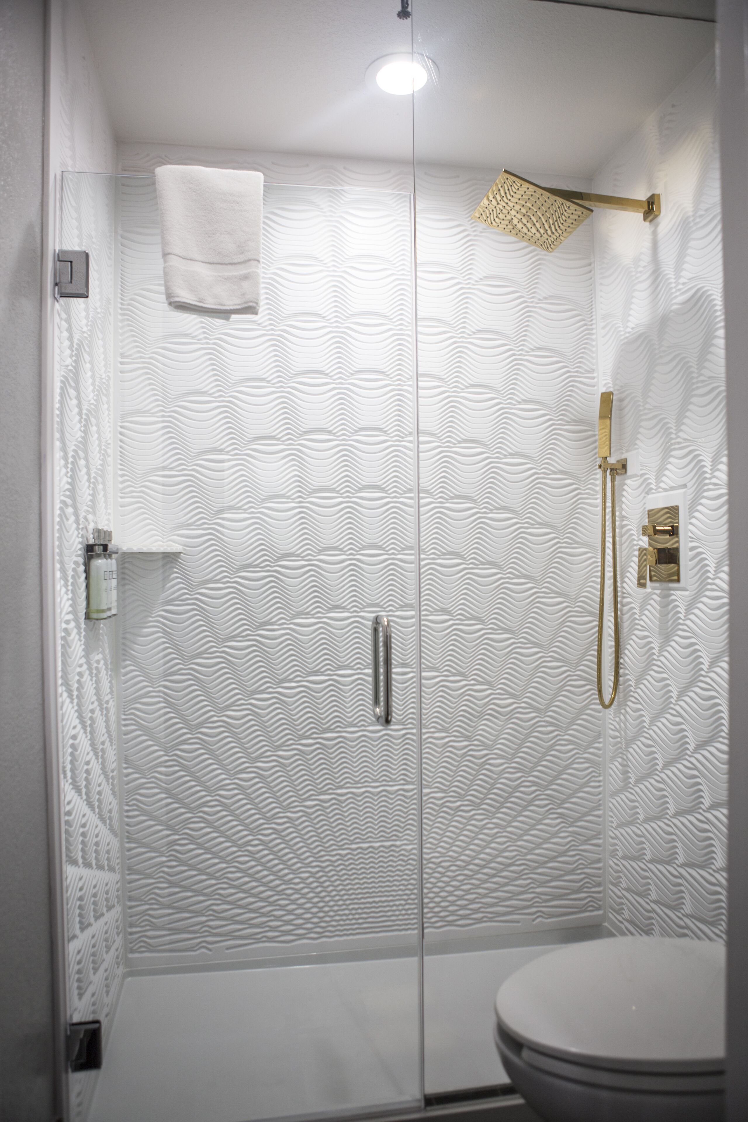 A modern bathroom with a glass shower enclosure, a toilet, and a towel hanging on the wall.