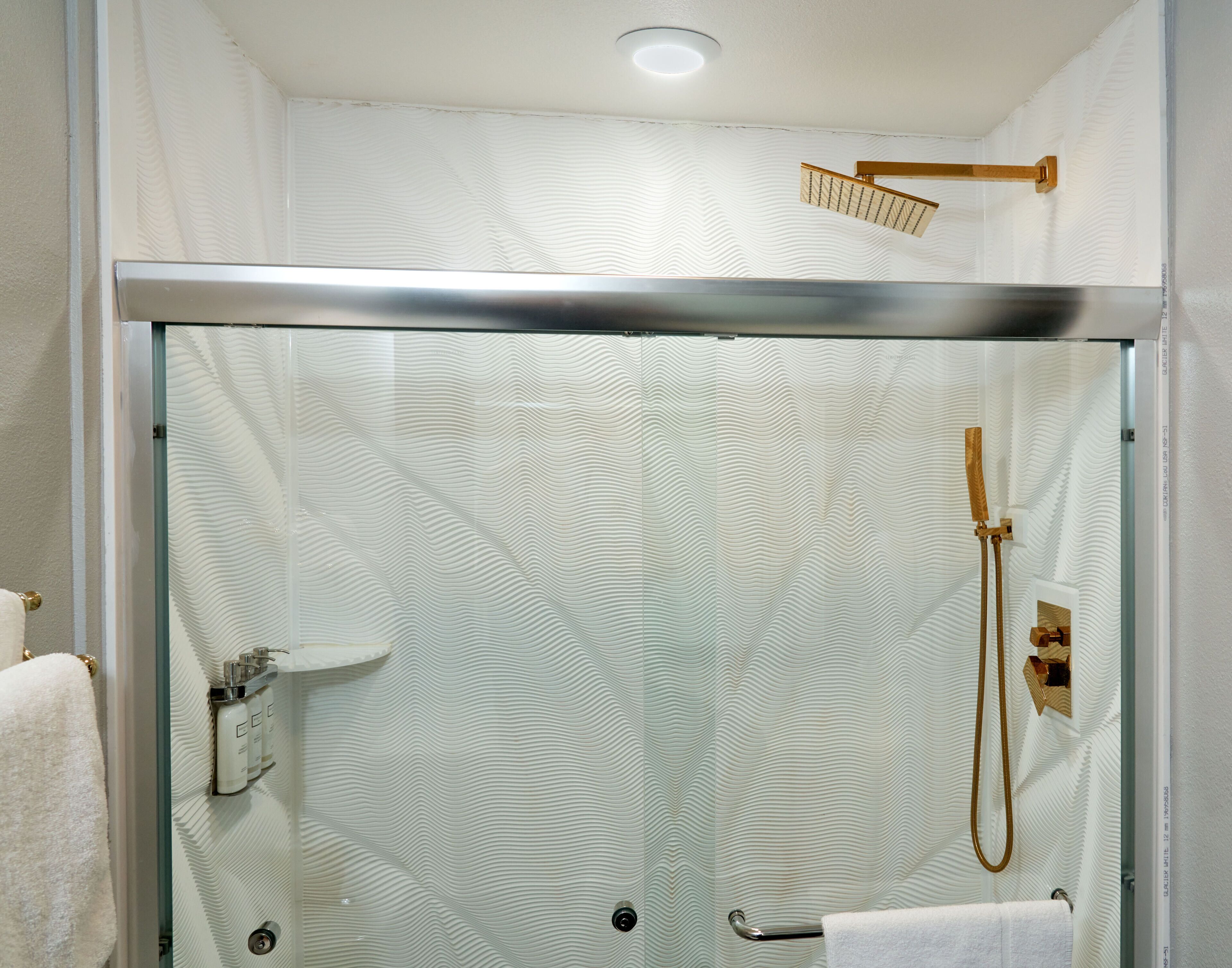 A glass-enclosed shower with a handheld showerhead and a wall-mounted faucet.