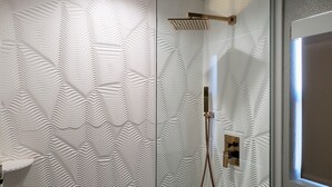 A bathroom with a textured wall, a shower with a gold showerhead, and a visible plumbing fixture.