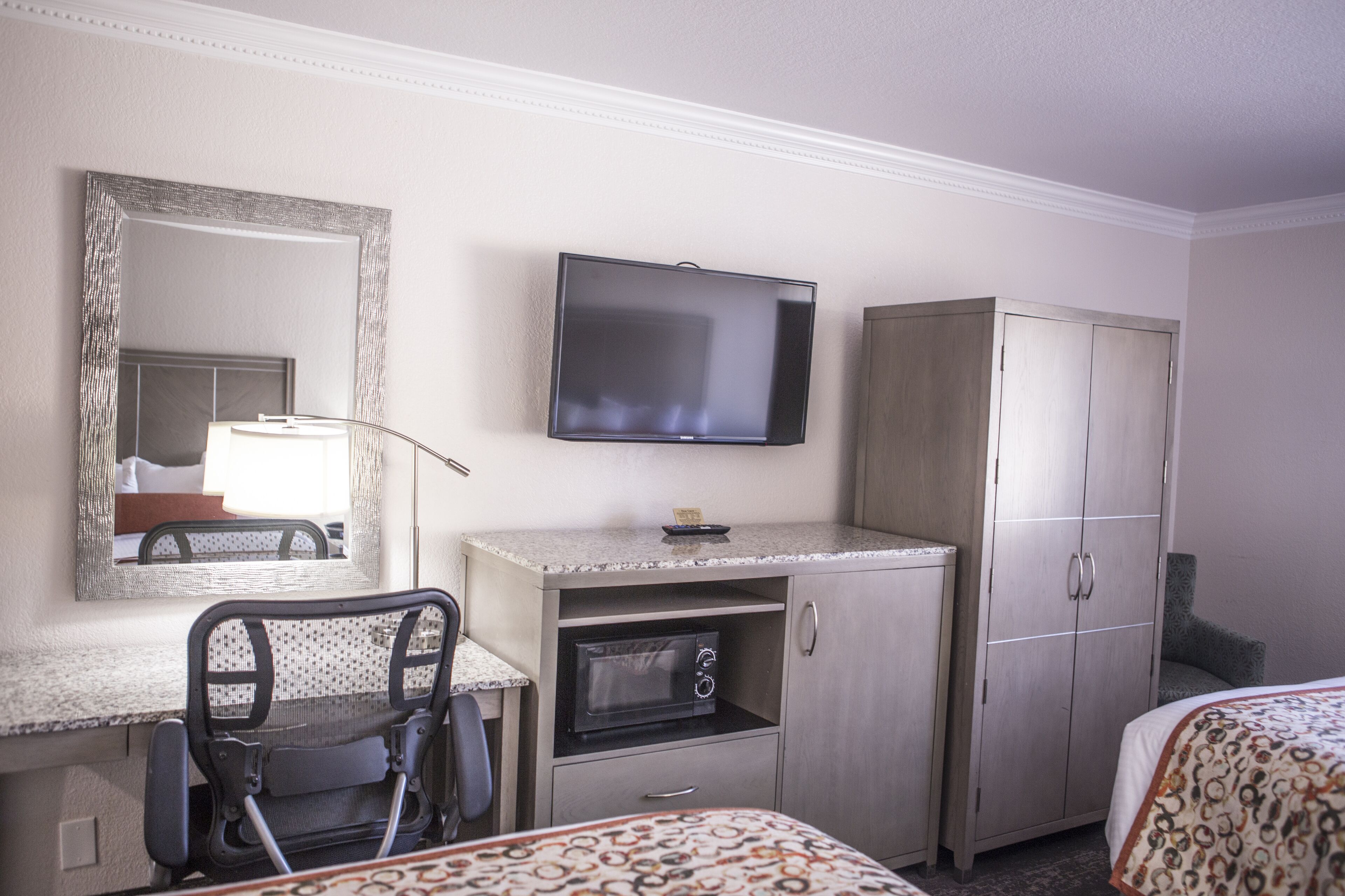 Habitación de hotel con cama, escritorio con silla, microondas, televisor y armario.