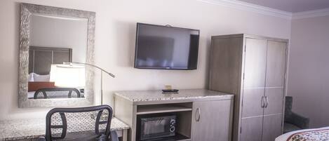 Habitación de hotel con cama, escritorio con silla, microondas, televisor y armario.