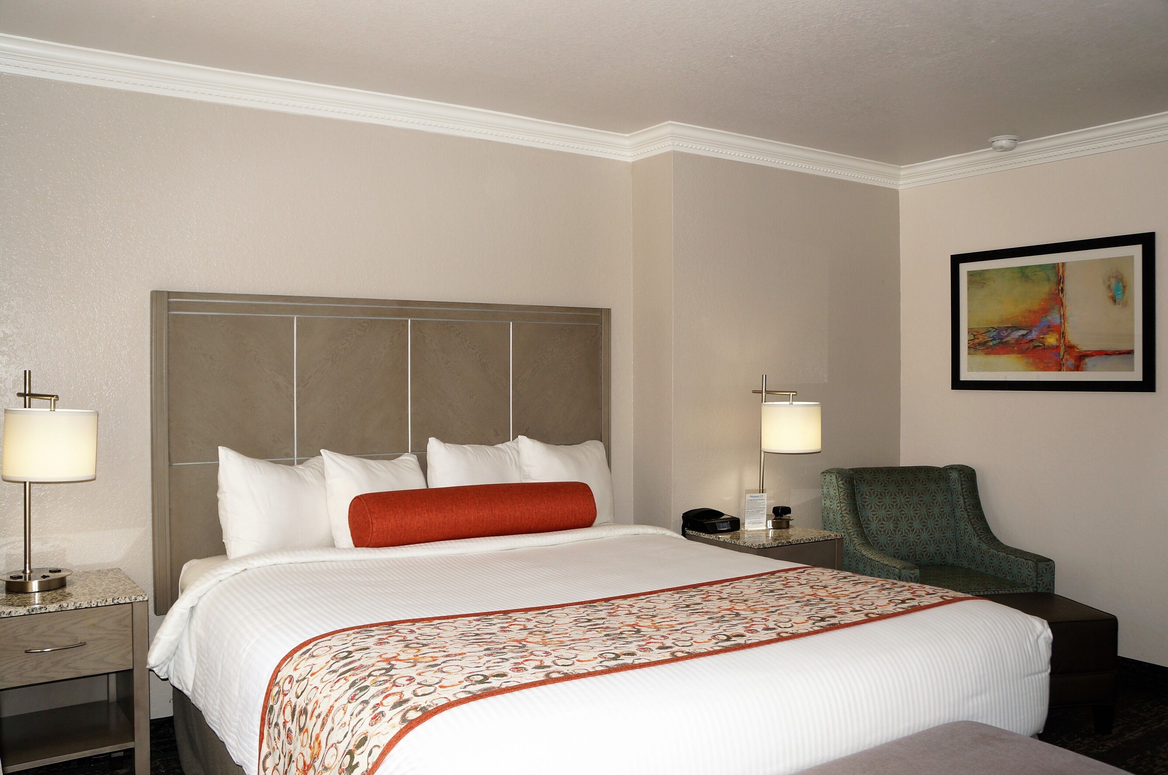 A hotel room with a large bed, two bedside tables, a chair, and a painting on the wall.