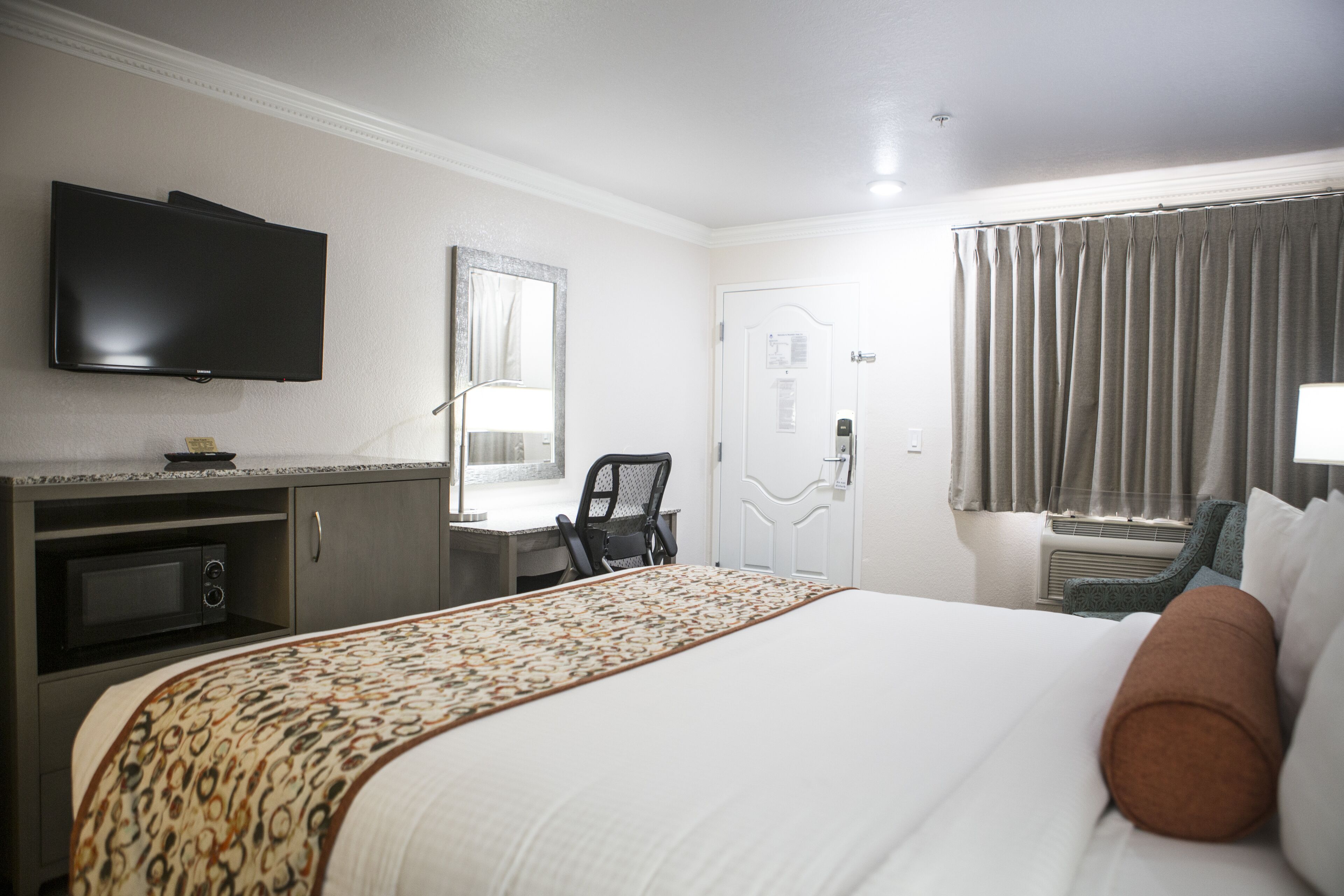 A hotel room with a bed, a desk, a chair, a television, and a window with curtains.