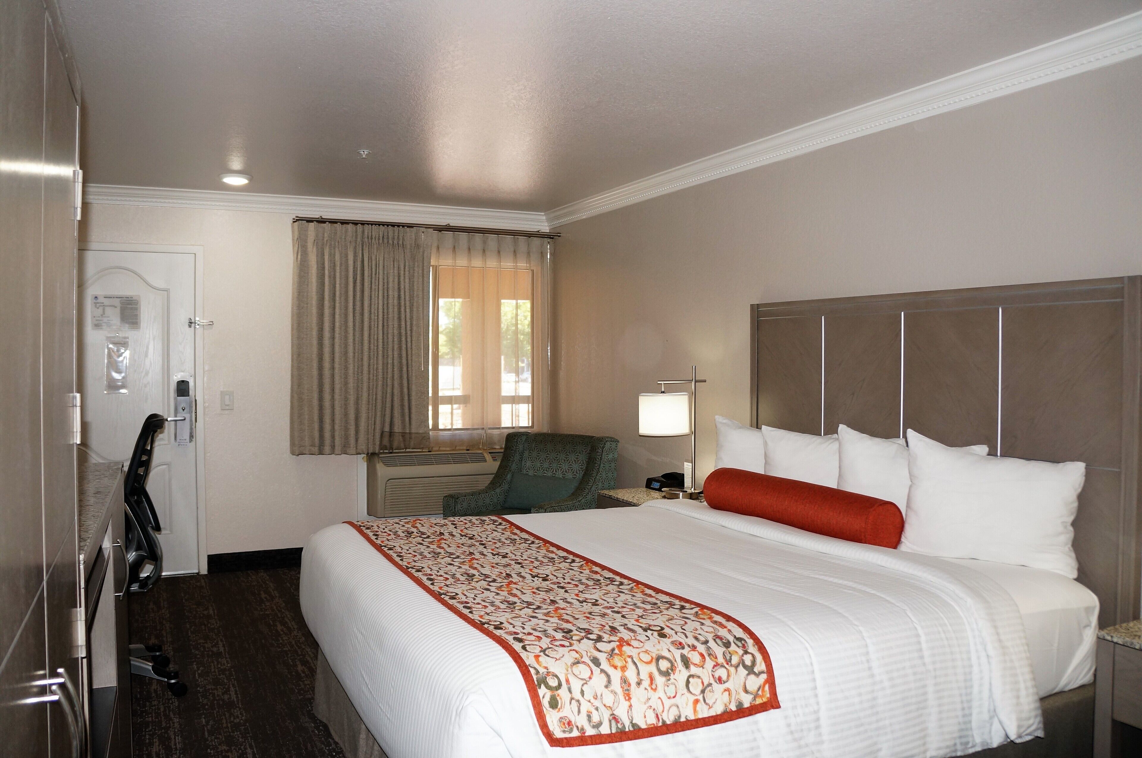 Habitación de hotel con una cama grande, un escritorio, una silla y una ventana con cortinas.