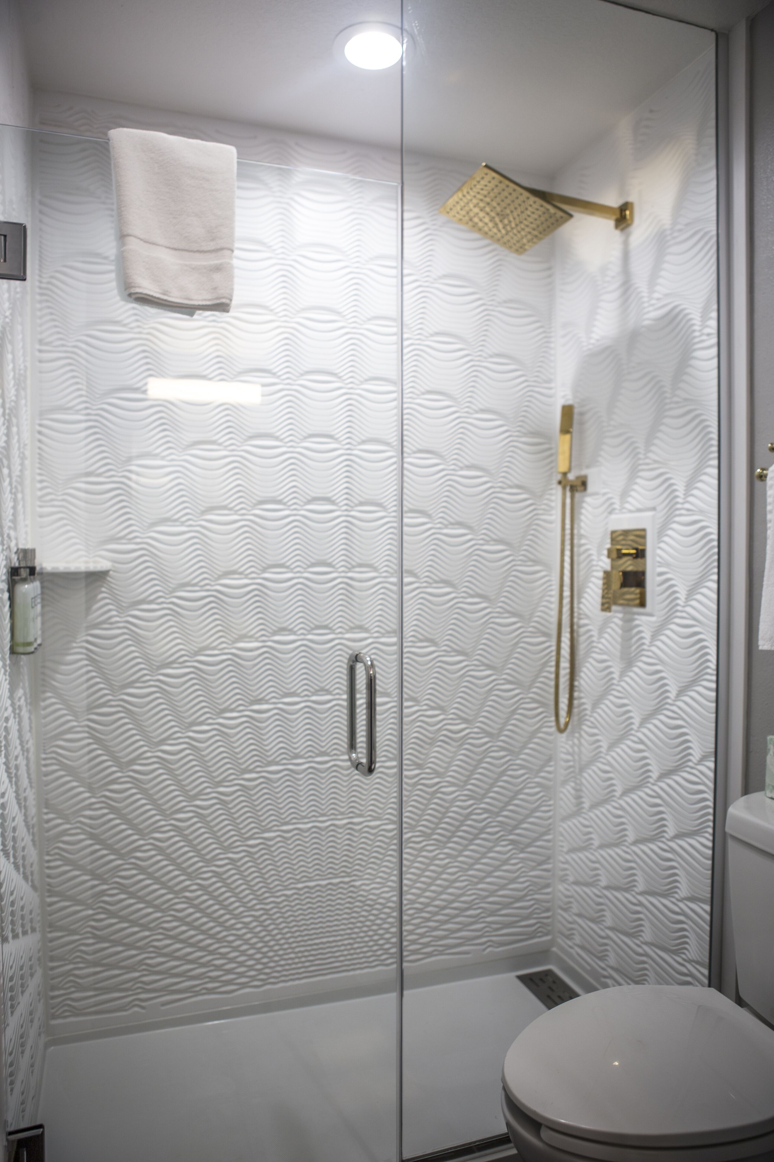 A modern bathroom with a glass shower enclosure, a toilet, and a towel hanging on the wall.