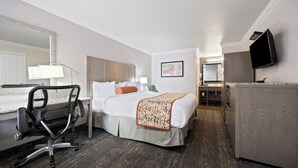 A hotel room with a bed, desk, chair, and a TV on the wall.
