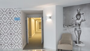 A hotel lobby with a patterned wall, a chair, a small table, and a hallway leading to another room. - Hotel Globales Cala Blanca (Ciutadella de Menorca)