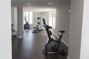 A spacious home gym with a variety of exercise equipment, including stationary bikes and a treadmill, in a well-lit room with large windows. - Hotel Globales Cala Blanca (Ciutadella de Menorca)