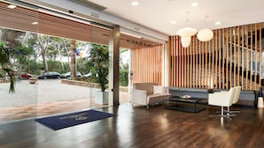 A modern lobby with a reception desk, seating area, and a view of parked cars outside.