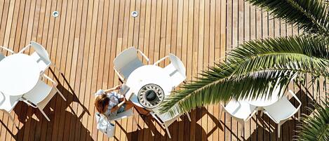 An outdoor seating area with a wooden deck, white tables, and chairs.