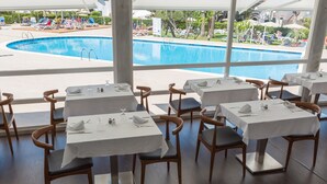 A restaurant with tables set for dining, overlooking a swimming pool. - Hotel Globales Cala Blanca (Ciutadella de Menorca)