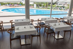 A restaurant with tables set for dining, overlooking a swimming pool. - Hotel Globales Cala Blanca (Ciutadella de Menorca)