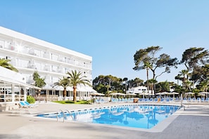 A hotel with a swimming pool, outdoor seating, and palm trees. - Hotel Globales Cala Blanca (Ciutadella de Menorca)